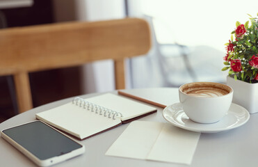 Close-up shot, latte coffee with mobile phone and note book on white table, relax in the morning in cafe before work