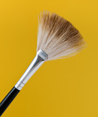 Close-up of a fan-shaped makeup brush with yellow background