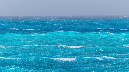 Vibrant blue water stretches out before you, with gentle, rolling waves creating a peaceful atmosphere. The water moves calmly, reflecting the bright sun above, and the entire scene exudes tranquility