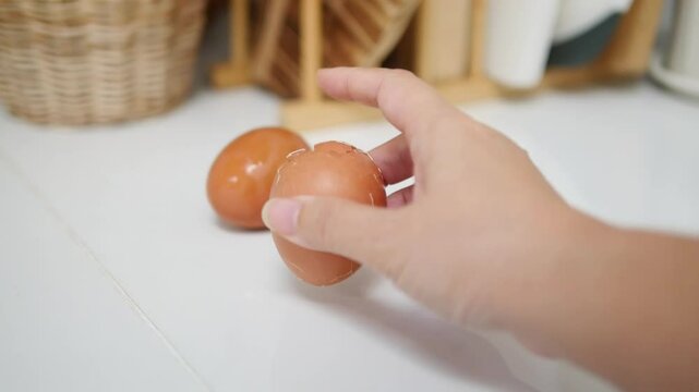 Close-up of hands cracking a brown egg on a white countertop, with wicker basket and blurred kitchen items in the background