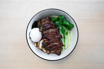 A bowl of noodles with beef, egg, and vegetables.