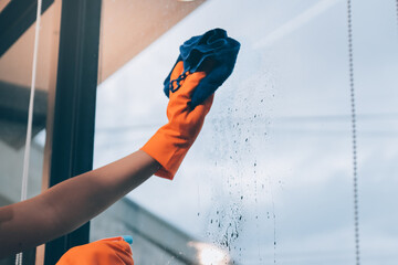 Young female worker cleaning window glass with cloth in spacious villa