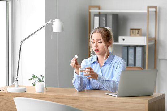 Young businesswoman with soluble tablet and glass of water in office