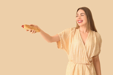 Pretty young woman with tasty french hot dog on beige background