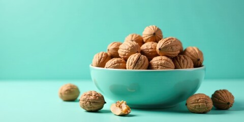 A Bowl of Shelled Walnuts on a Teal Background with Some Walnuts Scattered Nearby