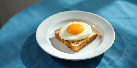 A perfectly fried egg sunny-side up atop a slice of toasted bread, served on a pristine white plate, rests on a textured blue surface.
