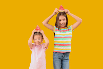 Happy little girls with slices of fresh watermelon on yellow background