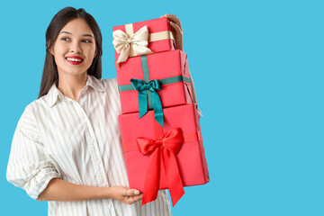 Beautiful young Asian woman with gift boxes on blue background