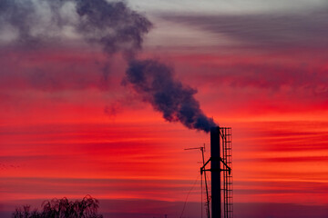Industrial chimney on sunrise background, red sky. Concept of beauty of nature and pollution