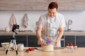 Young man with sweet cake and muffins recording cooking video in kitchen