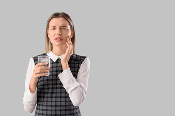 Young businesswoman with glass of cold water suffering from tooth ache on grey background