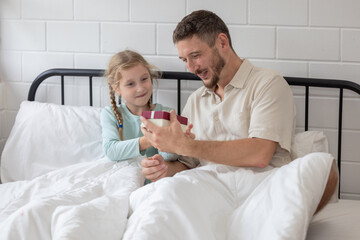 Obraz premium Father and daughter enjoy a joyful morning together as she surprises him with a gift in their cozy bedroom