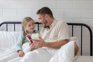 Obraz premium Father and daughter enjoy a joyful morning together as she surprises him with a gift in their cozy bedroom
