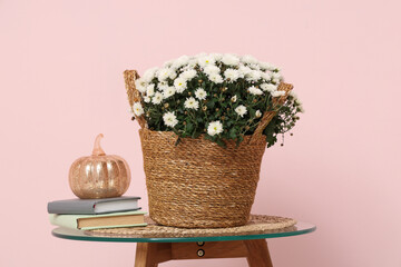 Wicker basket with chrysanthemum flowers and books on coffee table against pink background