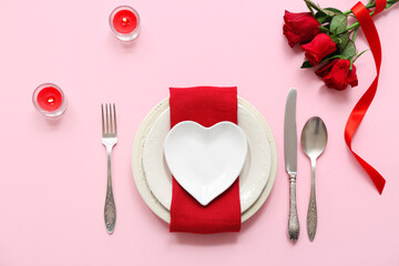 Beautiful table setting with red roses and burning candles on pink background. Valentine's Day celebration
