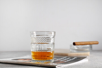 Glass of cold rum, cigar and magazine on table against grey background. Closeup
