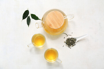 Glass cups and teapot of hot green tea with dried leaves on white background