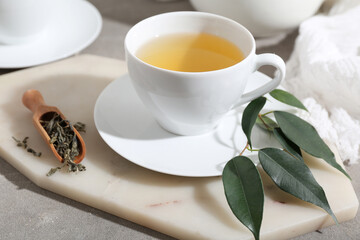 Cup of hot green tea and dried leaves on grey background