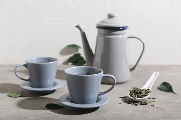 Cups and teapot of hot green tea with dried leaves on grey table
