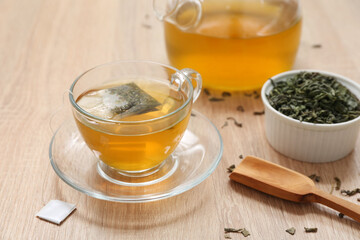 Glass cup of hot green tea and dried leaves on wooden background