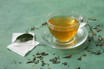 Glass cup of hot green tea and dried leaves on color background