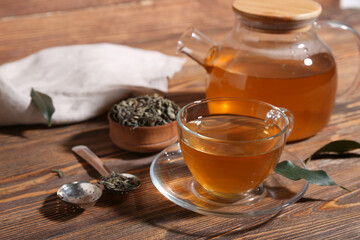 Glass cup and teapot of hot green tea with dried leaves on wooden background