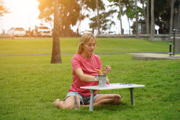 Young woman beading colorful bracelets outdoors in a park