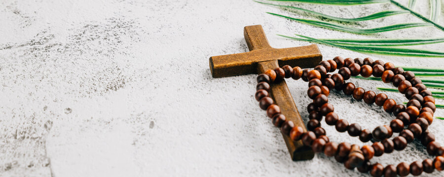 Palm frond, wooden cross, and rosary beads on a gray background for Sunday. Highlighting Easter holiday traditions