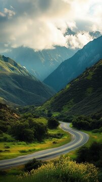 Carretera sinuosa entre colinas verdes y monta&ntilde;as envueltas en nubes bajo un cielo parcialmente nublado