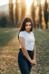 The woman is wearing a white T-shirt and dark jeans with a belt. The light falls from behind, creating soft lighting and a warm atmosphere.