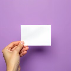 Fototapeta premium A hand holds a blank white card against a purple background. Perfect for your message or design mockup.