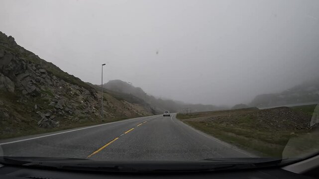 Driving through the tundra in northern Norway on E69 road. Misty scenery with rocky hills, a small lake, and few houses, creating a tranquil and remote atmosphere.