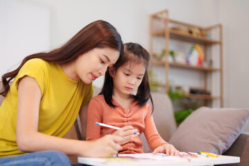 A mother assisting her daughter with homework at the table, surrounded by books and stationery,...