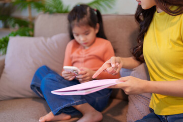 A mother scolding her daughter for excessive phone usage while sitting together on the sofa, focusing on discipline and balance.