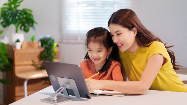 A mother is teaching her young daughter to do homework together at the table, creating a supportive and educational environment.