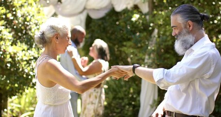 Dancing together, senior bride and groom enjoying outdoor wedding event with friends in background - Powered by Adobe