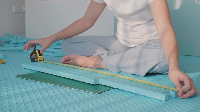 A person measures foam materials with a tape measure while sitting on a blue surface, preparing for a crafting project. The workspace appears organized and creative, showcasing tools and materials rea