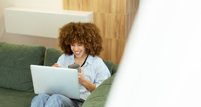 Young woman enjoys a cozy moment with her laptop in a stylish modern living space during a sunny afternoon - Powered by Adobe