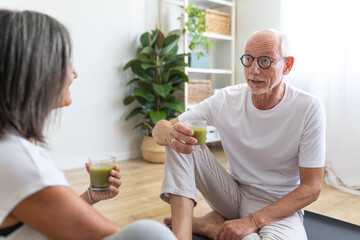 Mature caucasian man drinking healthy green juice after exercising with wife at home