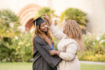 Mother reaching up to fix graduate daughters cap and gown