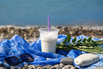 a milkshake in a disposable plastic cup with a straw On the background of the blue sea. Healthy lifestyle