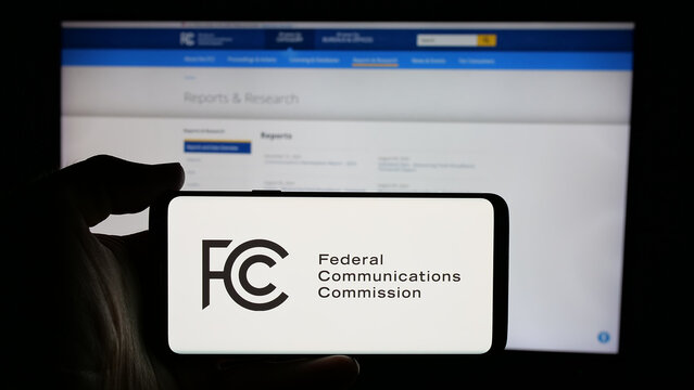 Stuttgart, Germany - 01-23-2025: Person holding cellphone with logo of US agency Federal Communications Commission (FCC) on screen in front of webpage. Focus on phone display.