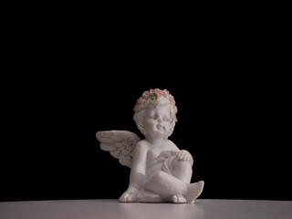 A white angel statue with a flower crown on its head sits on a black table