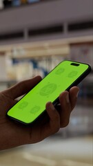 GREEN SCREEN CHROMA KEY Smartphone with a green screen held in a hand inside a shopping center, ideal for app, tech, or retail marketing visuals