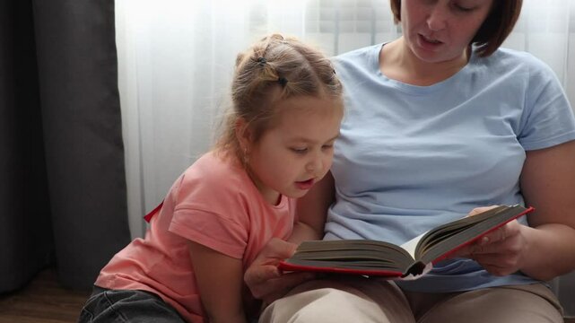 Close up of happy mother and Caucasian little daughter are reading book of fairy tales together. Concept of Mother's Day and preschool education