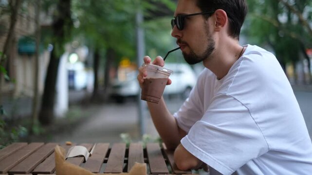 young brunette man drinks cappuccino on the terrace in a cafe on a hot summer day