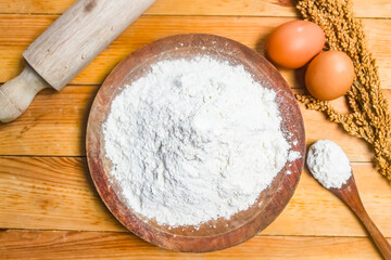 flour in a wooden bowl with eggs and a rolling pin beside it.