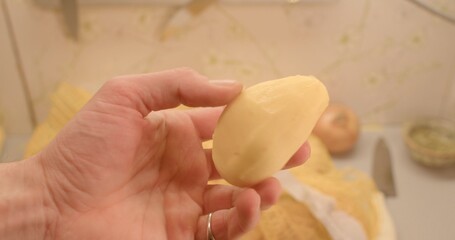 In a cozy kitchen setting, I hold a peeled potato in my hand, surrounded by a sharp knife and various fresh ingredients, capturing a delightful cooking preparation scene