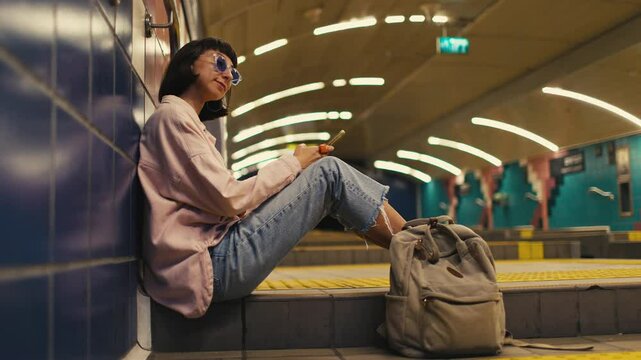 girl is waiting for the train and using the phone. girl on the subway. A young girl in stylish clothes with a backpack in the subway. fashion and style.