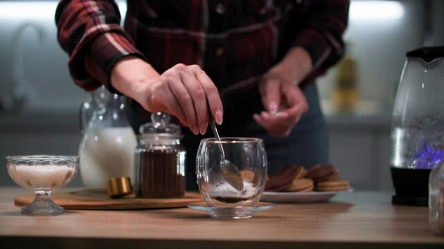 young woman in morning preparing hot coffee drink stirring coffee in cup and pouring milk on kitchen table, close up